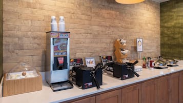 Una estación de café con una máquina de café, espumador de leche y una vitrina de pasteles.