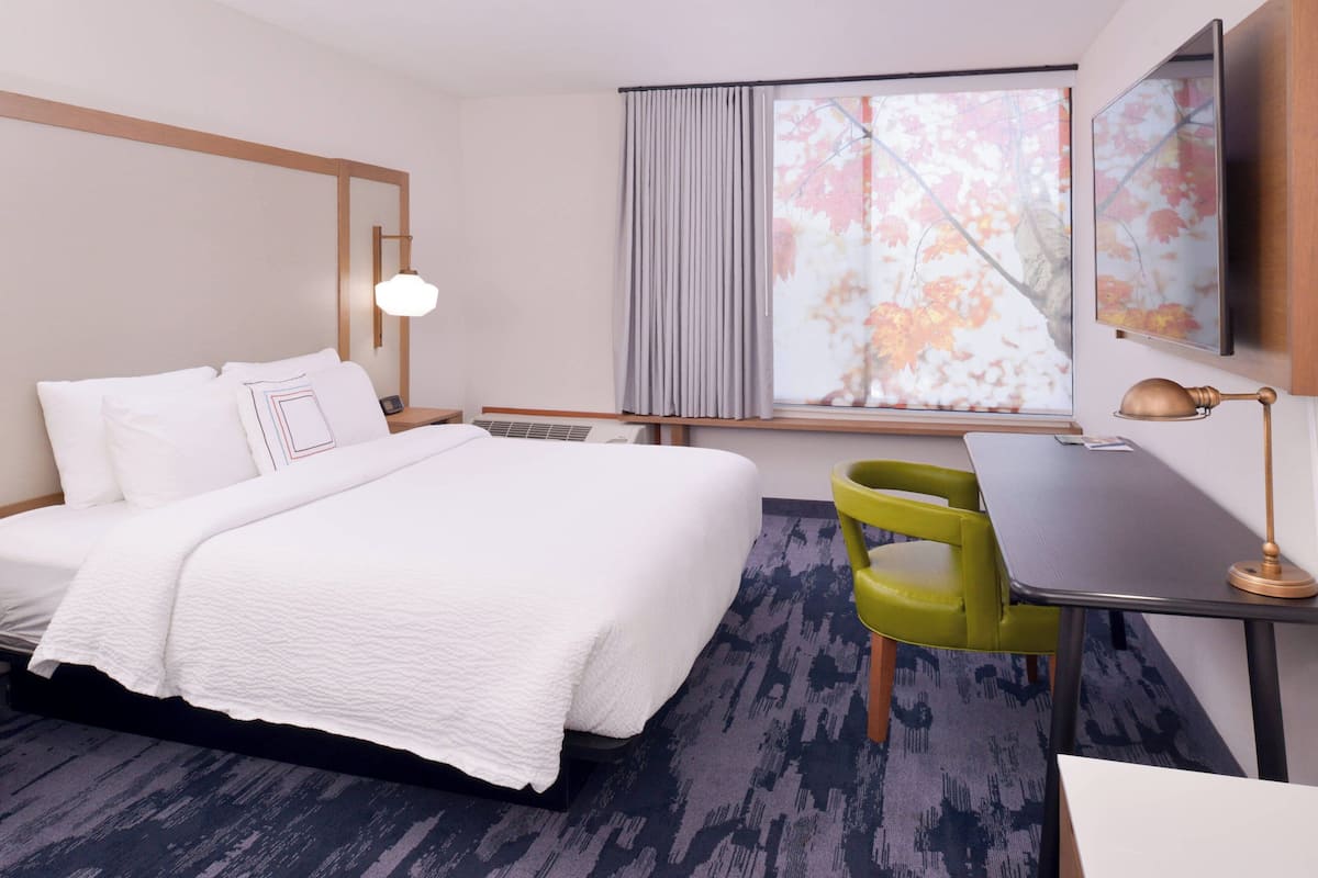 Hotelkamer met een bed, een bureau, een stoel, een raam met gordijnen en een tv aan de muur.
