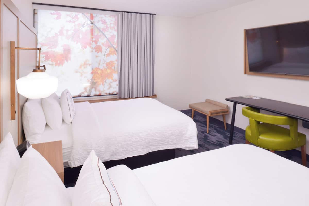 Een hotelkamer met twee bedden, een bureau, een stoel, een televisie en een raam met gordijnen.