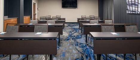 A conference room with a large screen, multiple tables, and a patterned carpet.