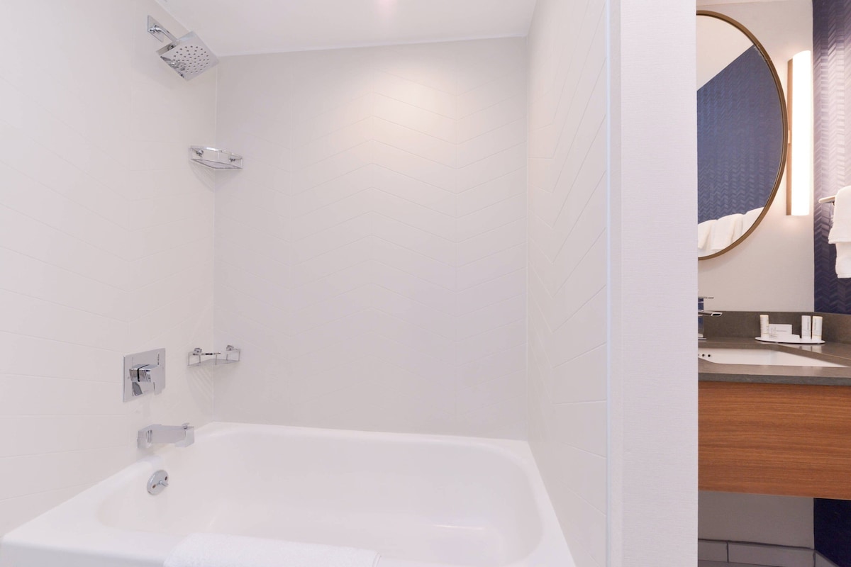 A modern bathroom with a white bathtub, a showerhead, and a vanity with a mirror.