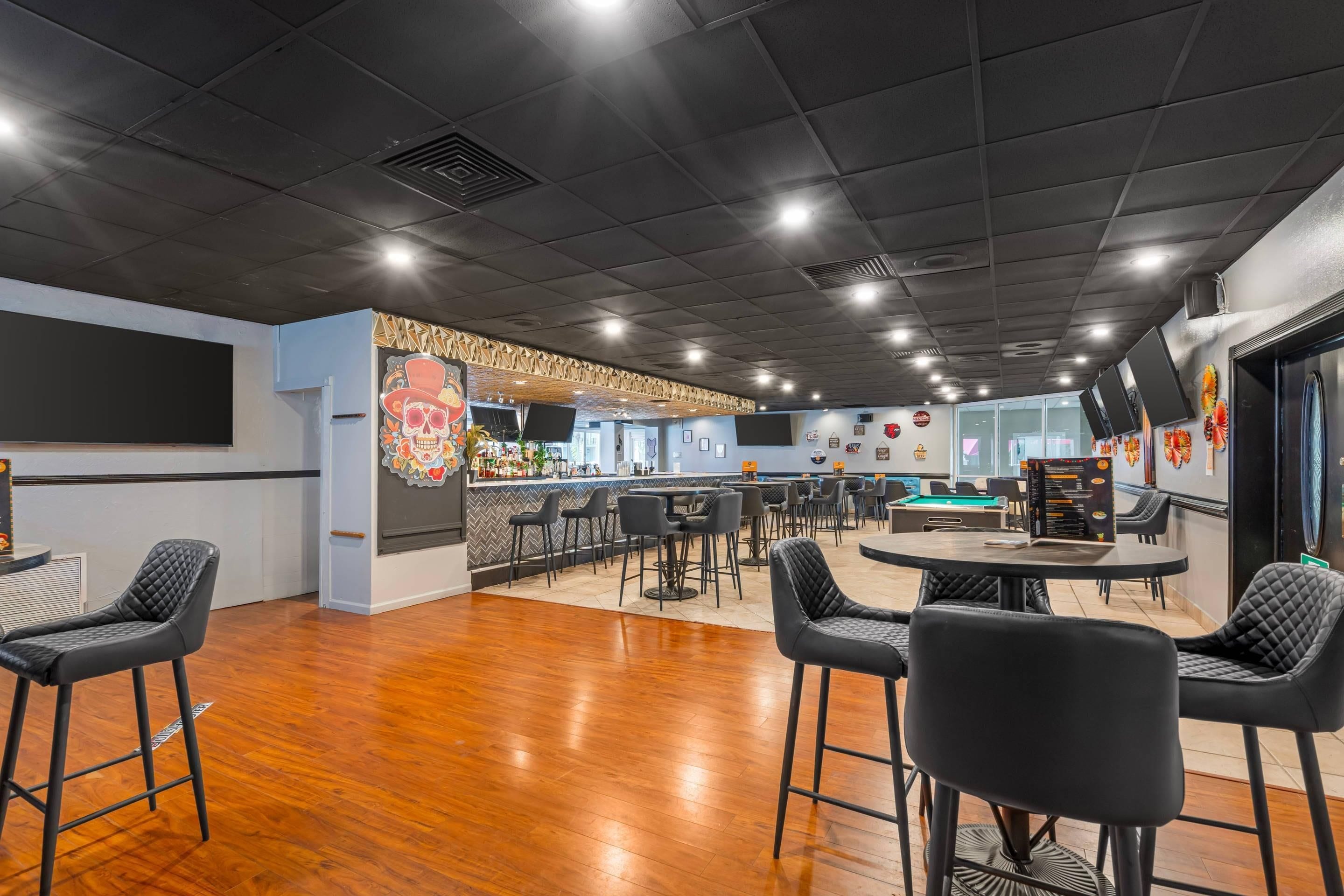 A modern bar area with wooden flooring, black bar stools, and a counter with a decorative skull mural.