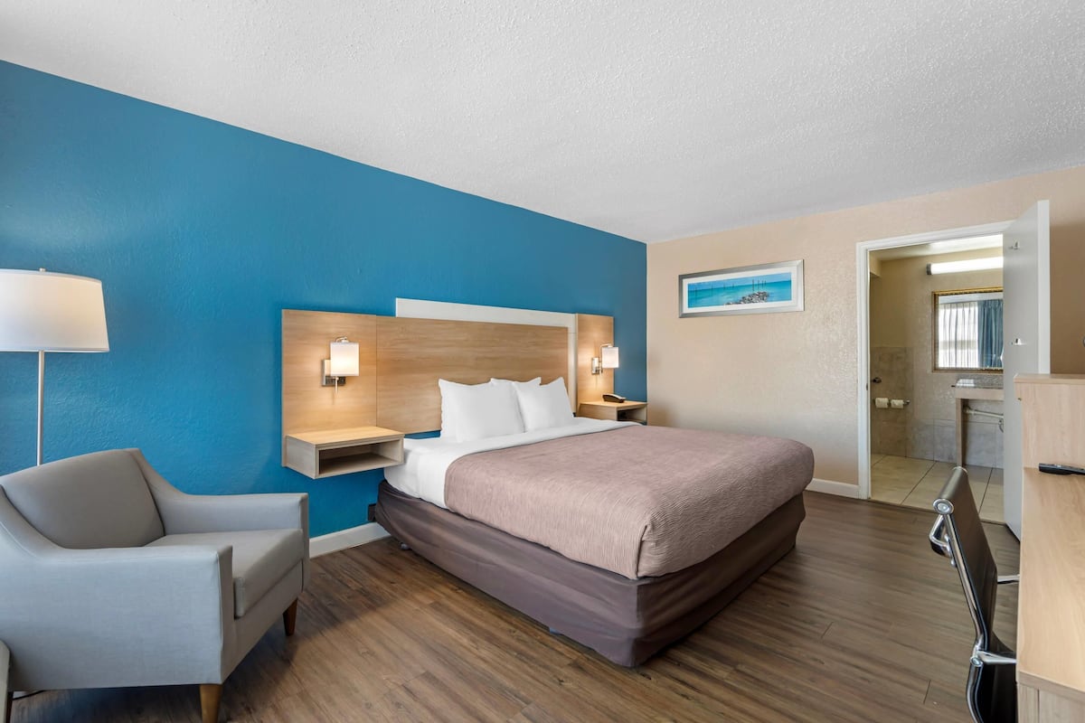 A hotel room with a large bed, a chair, a desk, and a bathroom visible through an open door.