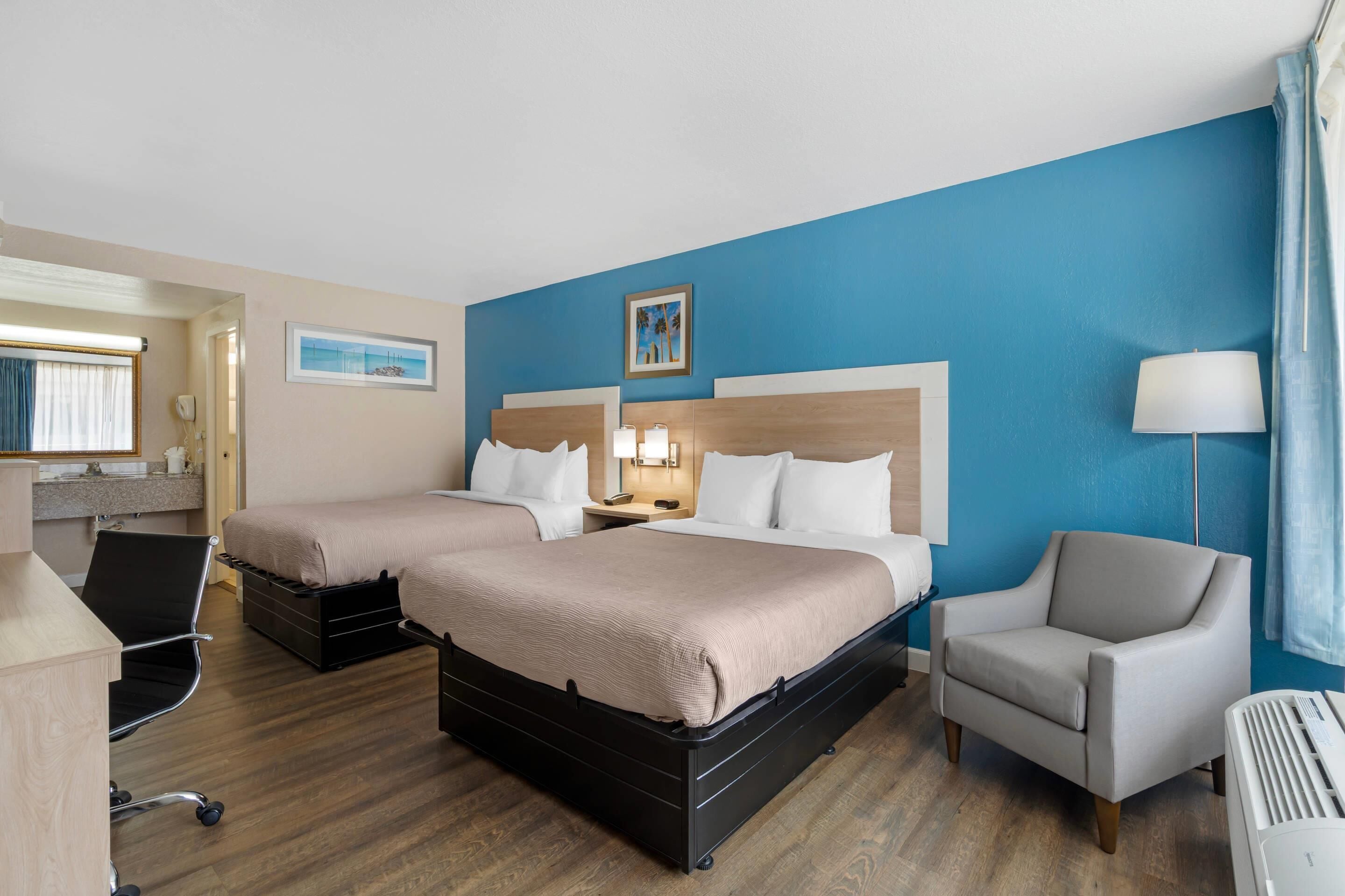Ein Hotelzimmer mit zwei Betten, einem Schreibtisch, einem Stuhl und einer Lampe.