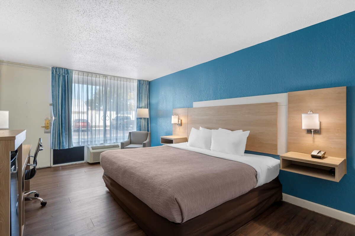 Une chambre d’hôtel avec un grand lit, un bureau, une chaise et une fenêtre avec des rideaux.