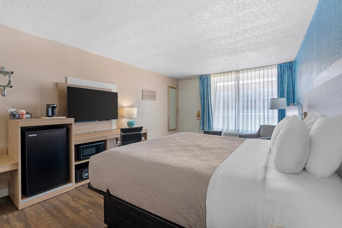 A hotel room with a bed, a TV, a minibar, and a desk with a lamp.