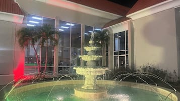Stunning outdoor space features a multi-tiered fountain and a circular pool surrounded by a low wall and palm trees.