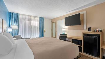 Ein Hotelzimmer mit einem großen Bett, einem flachbildfernseher an der Wand, einem Schreibtisch mit Computer und Kaffeemaschine sowie einem Minikühlschrank.