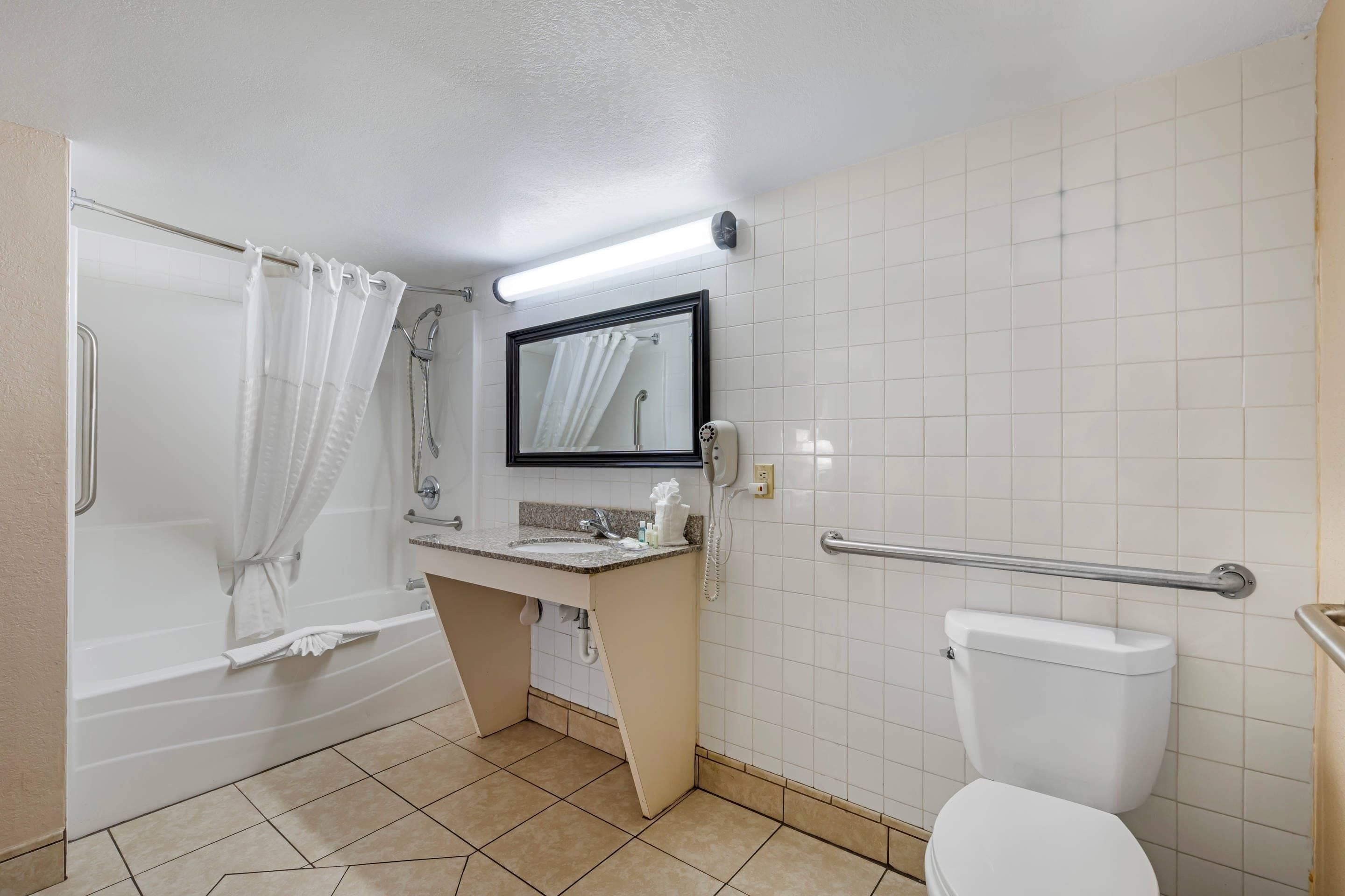 Et badeværelse med badekar, toilet, vask og et spejl.