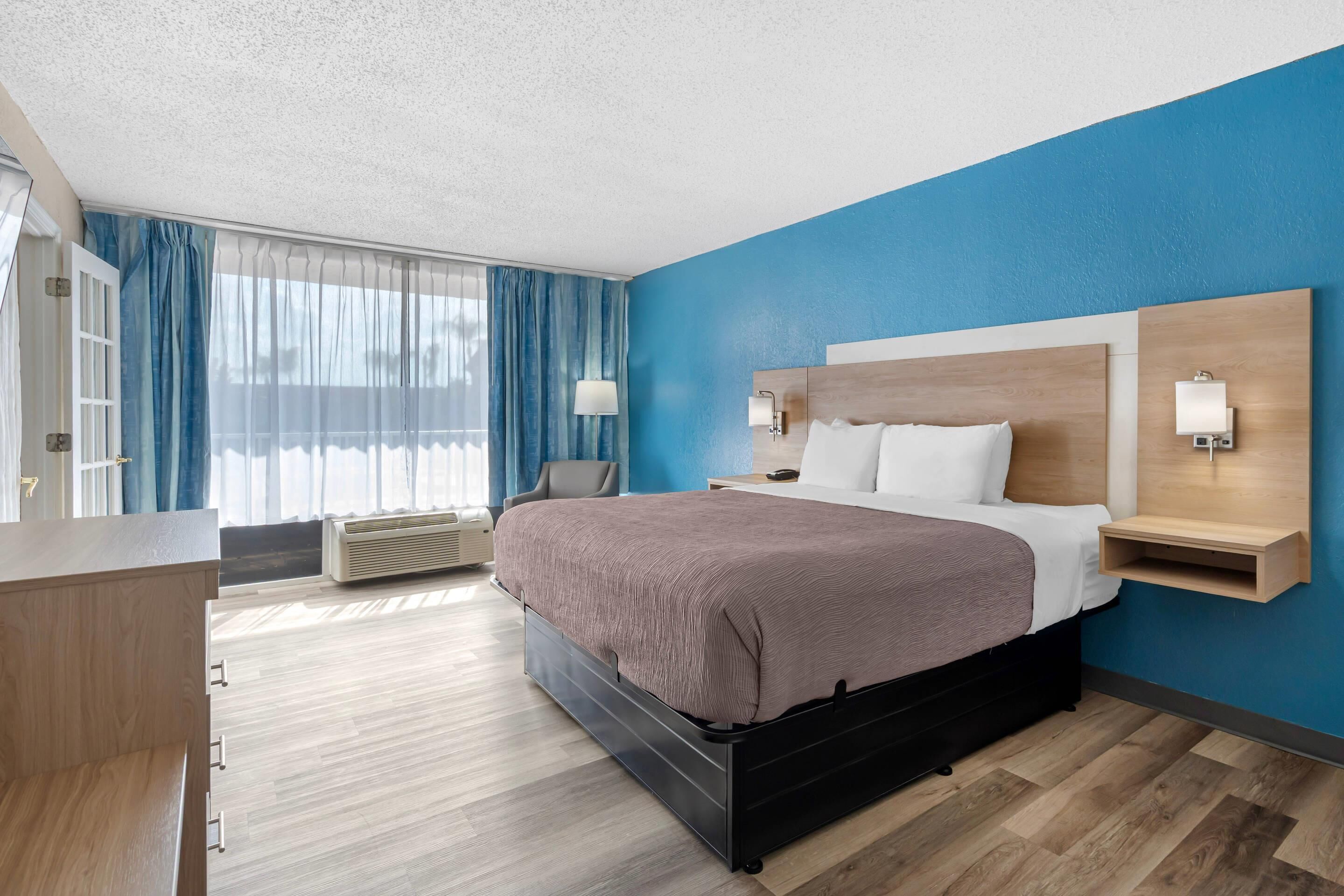 A modern hotel room with a large bed, a desk, and a chair.