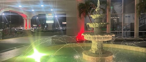 A night-time view of a hotel with a fountain in the foreground and a sign for "Quality" hotel suites in the background.