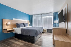 A modern hotel room with a bed, bedside table, lamp, and a TV mounted on the wall.