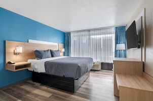 Una habitación de hotel moderna con cama, mesita de noche, lámpara y televisor montado en la pared.