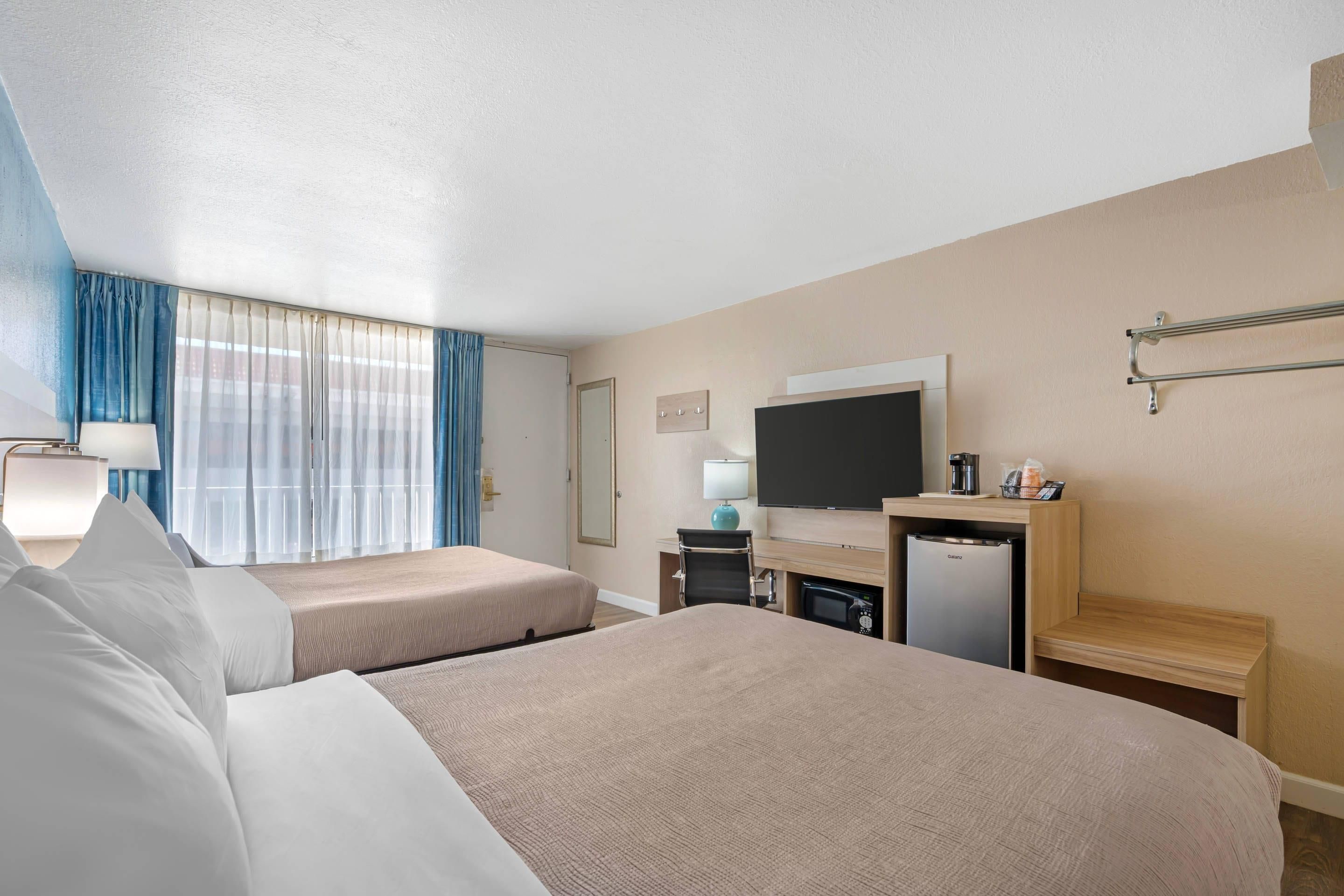 A hotel room with two beds, a TV, a desk with a computer, and a minibar.