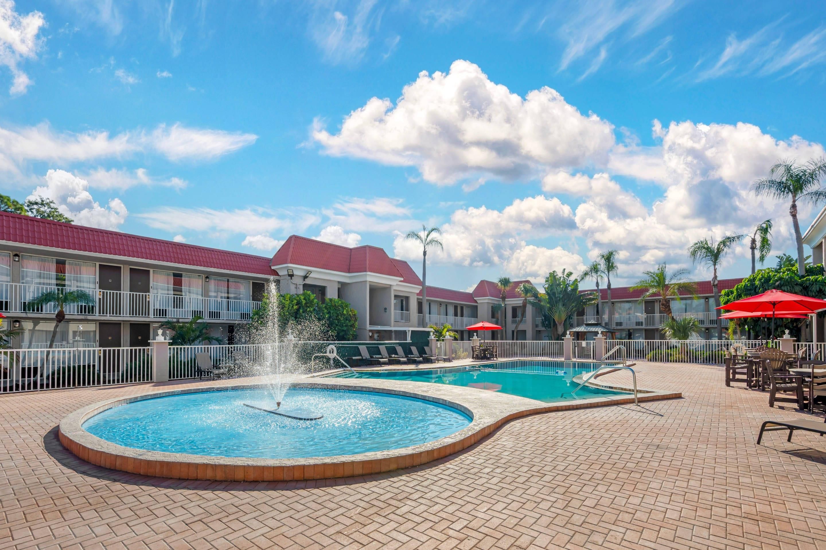 A hotel pool area with a circular hot tub, a rectangular pool, and lounge chairs.