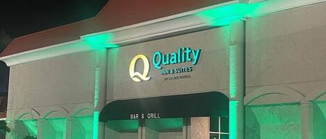 A hotel entrance with a sign reading "Quality Inn & Suites by Civiice Hotels" and a "BAR & GRILL" sign below.
