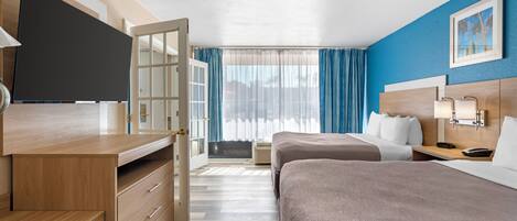 A hotel room with two beds, a desk with a flat-screen TV, a dresser, and a window with curtains.