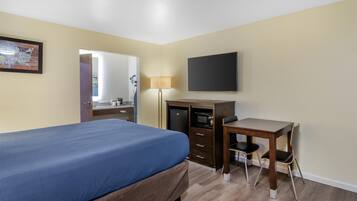 A hotel room with a bed, a desk, a chair, a television, a lamp, and a wardrobe.