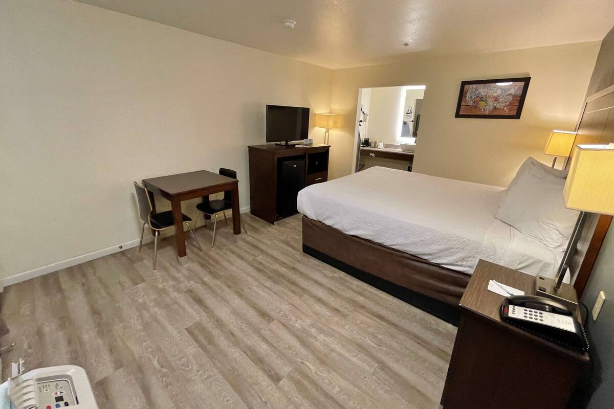 A hotel room with a bed, a desk, a television, a mirror, and a telephone.