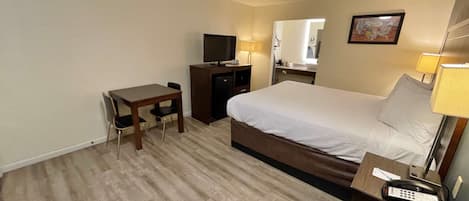 A hotel room with a bed, a desk, a television, a mirror, and a telephone.