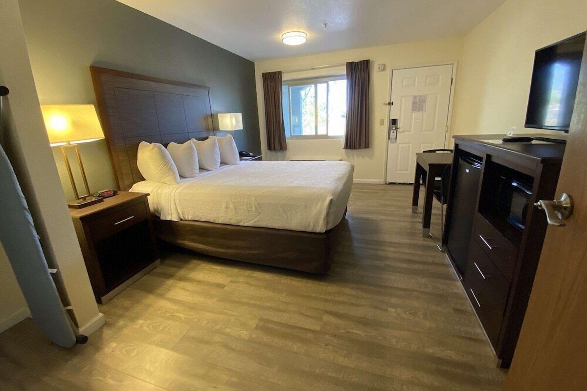 A hotel room with a bed, bedside tables, a desk, a television, and a window with curtains.