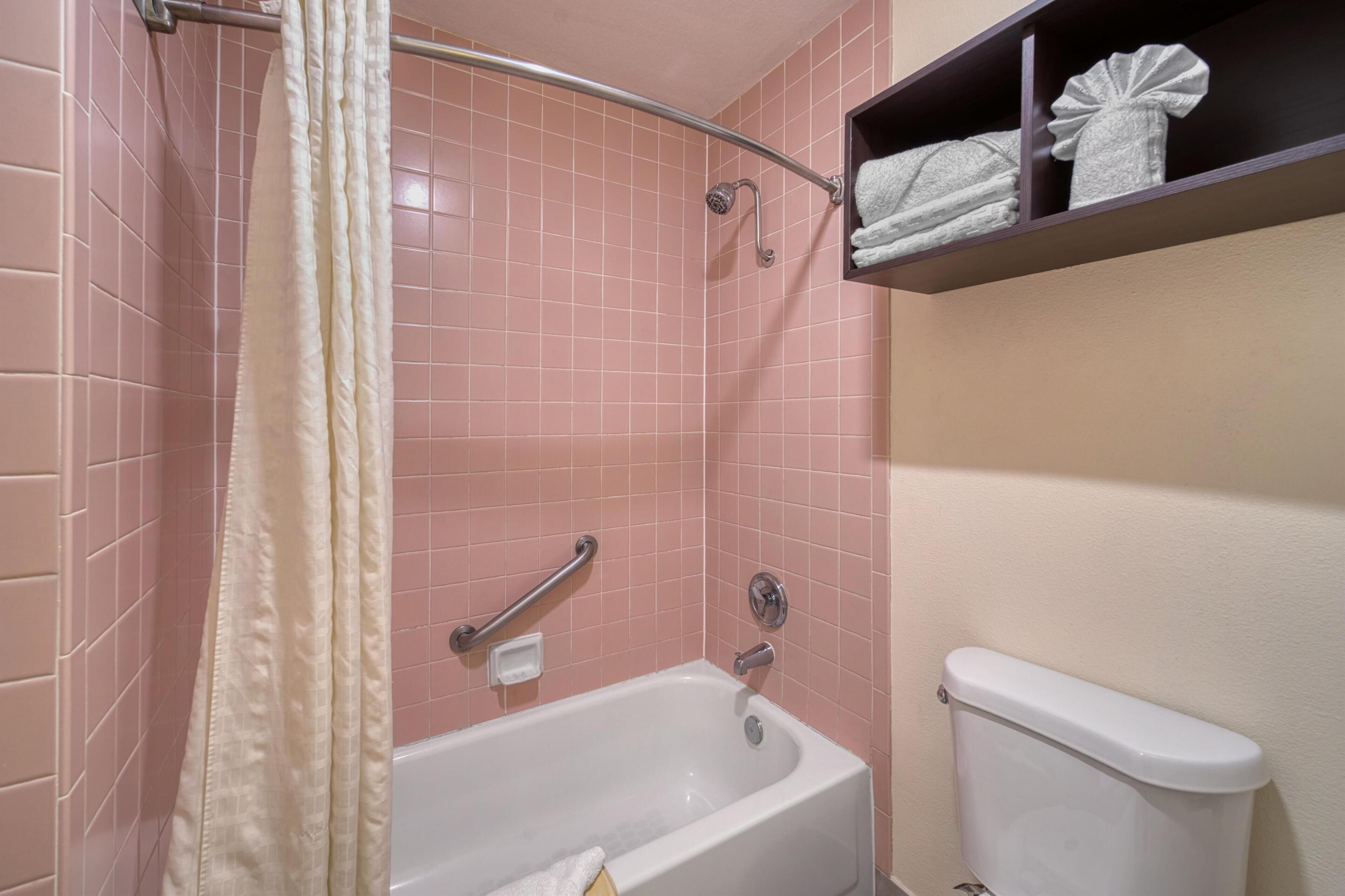 A bathroom with pink tiles, a white bathtub, a toilet, and a shelf with towels.