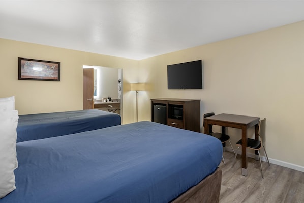 Habitación de hotel con dos camas, un escritorio, un televisor y un espejo.