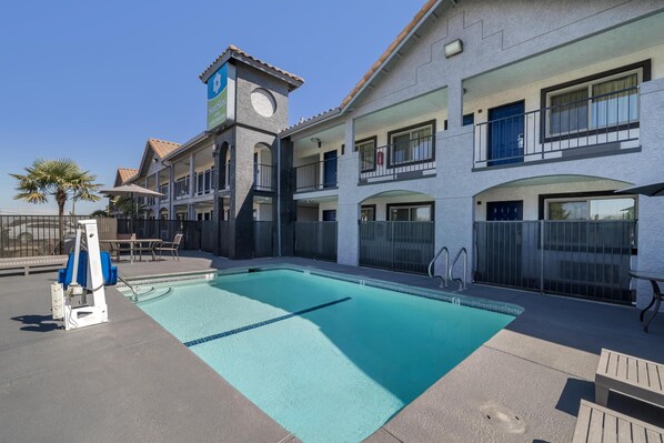 A pool area with a lifeguard stand, lounge chairs, and a building with a clock tower.