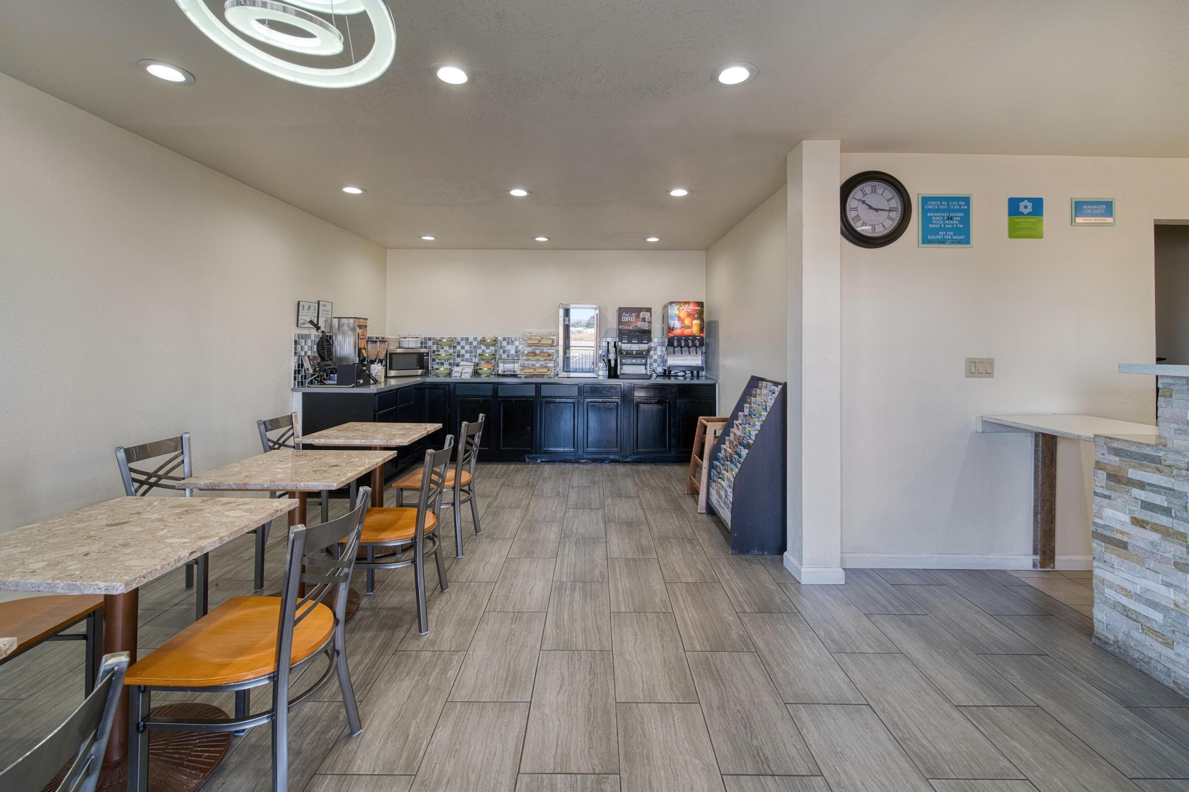 Une cuisine spacieuse dotée d’un îlot central, un coin repas avec des tables et des chaises, et une horloge au mur.