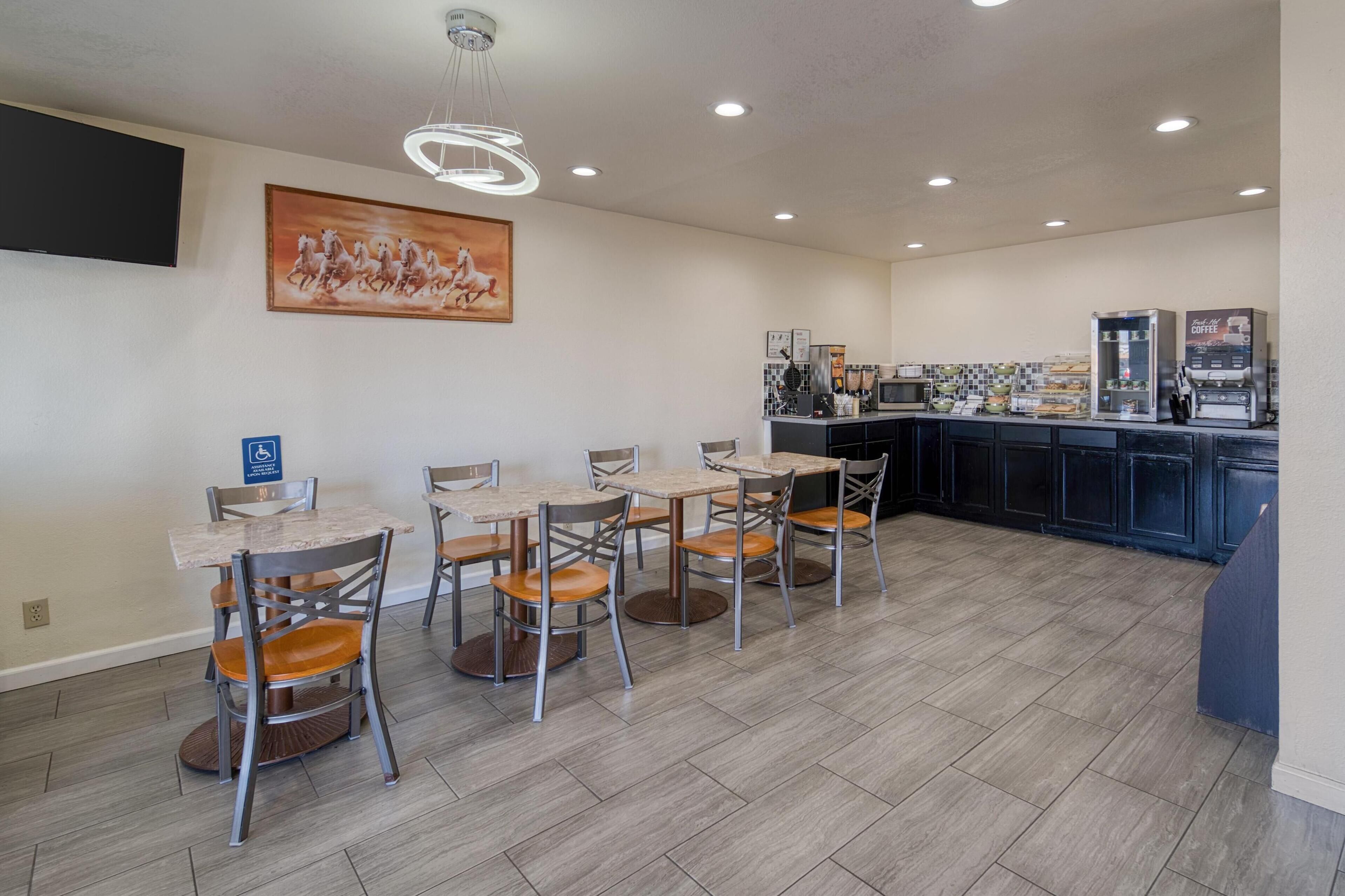 A dining area with six tables and chairs, a kitchen area with a coffee machine, and a mounted TV.