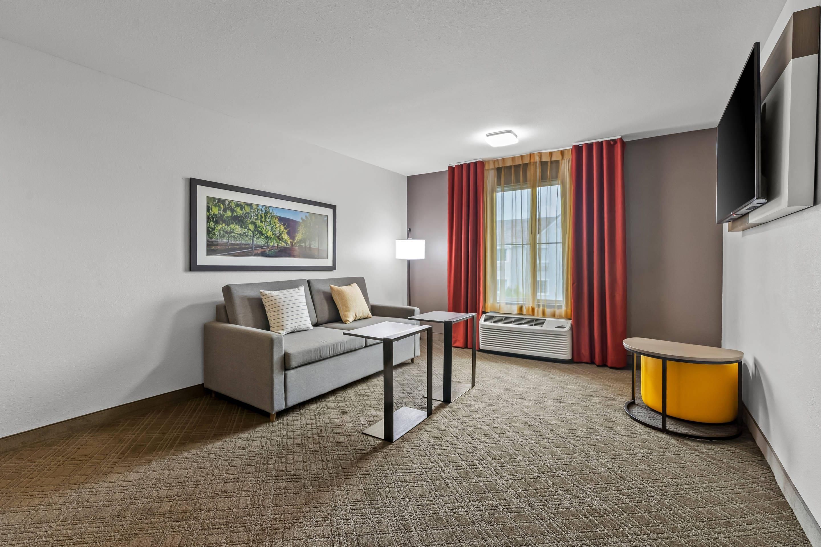 Habitación de hotel con sofá, una mesita, lámpara, televisor y ventana con cortinas.