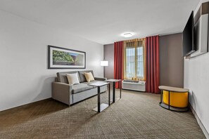 Een hotelkamer met een bank, een bijzettafeltje, een lamp, een televisie en een raam met gordijnen.