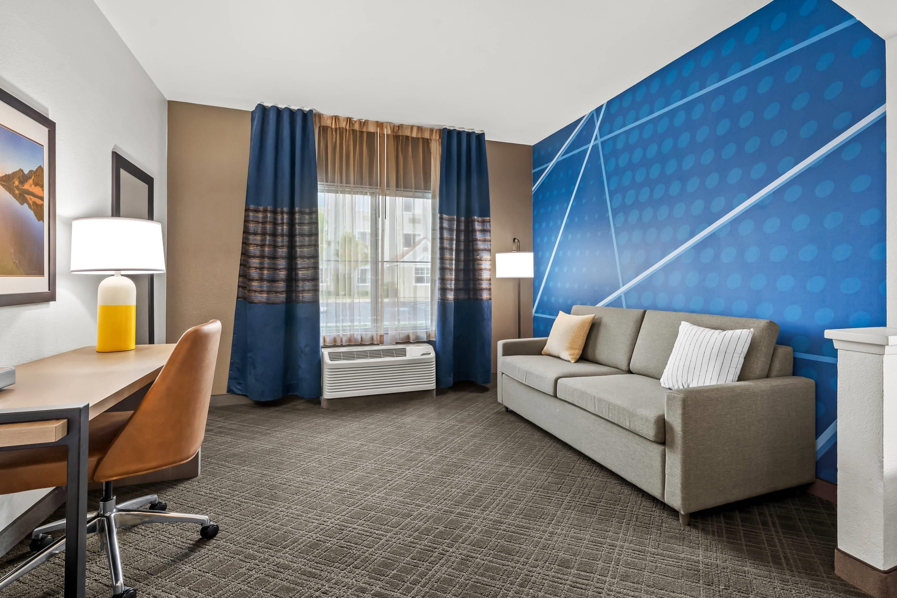 Een hotelkamer met een bureau, stoel, bank en een groot raam met gordijnen.