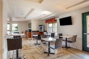 A modern dining area with bar seating, a flat-screen TV, and a kitchen in the background.