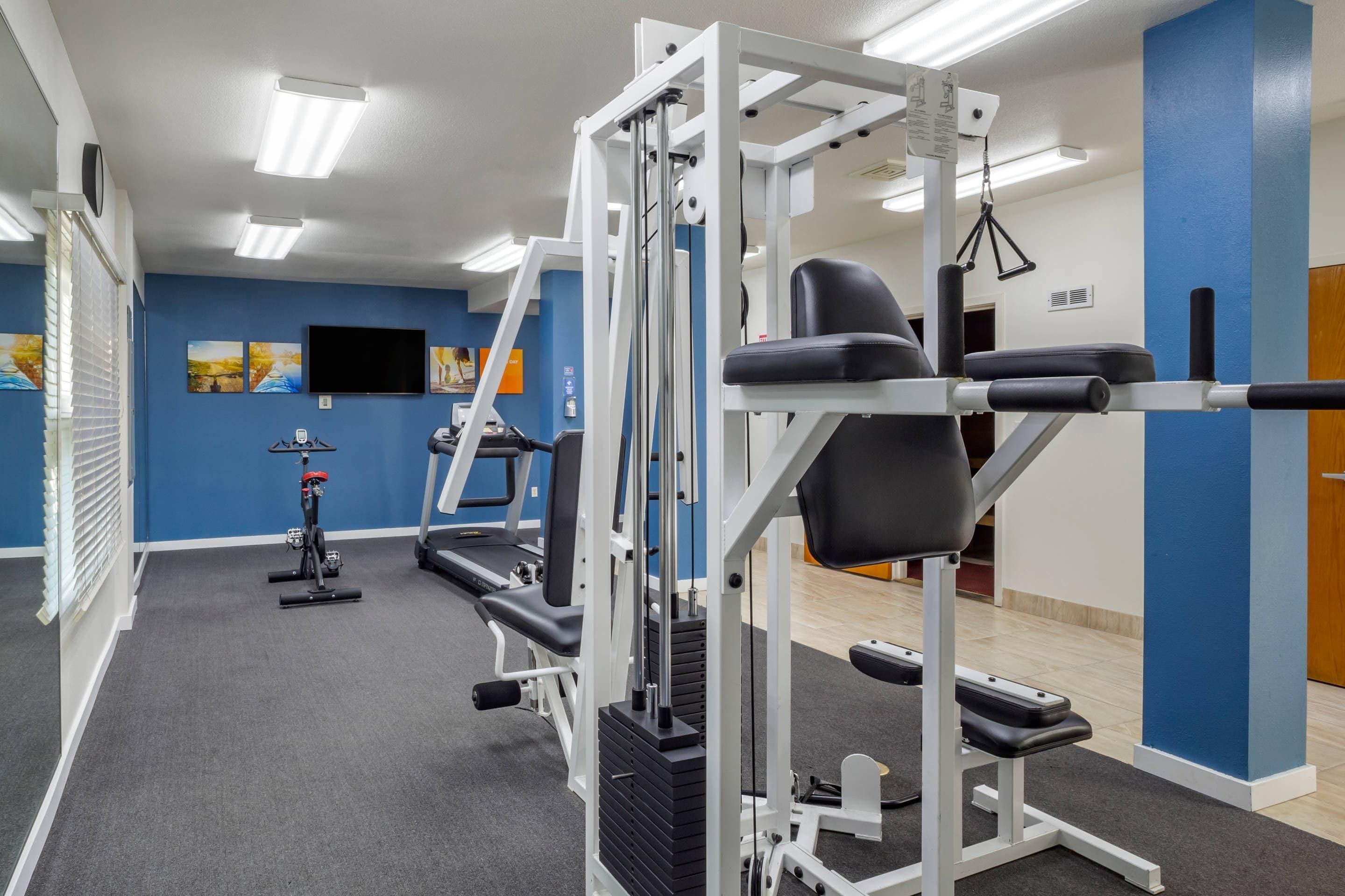Een sportschool met trainingsapparatuur, een loopband en een televisie aan de muur.