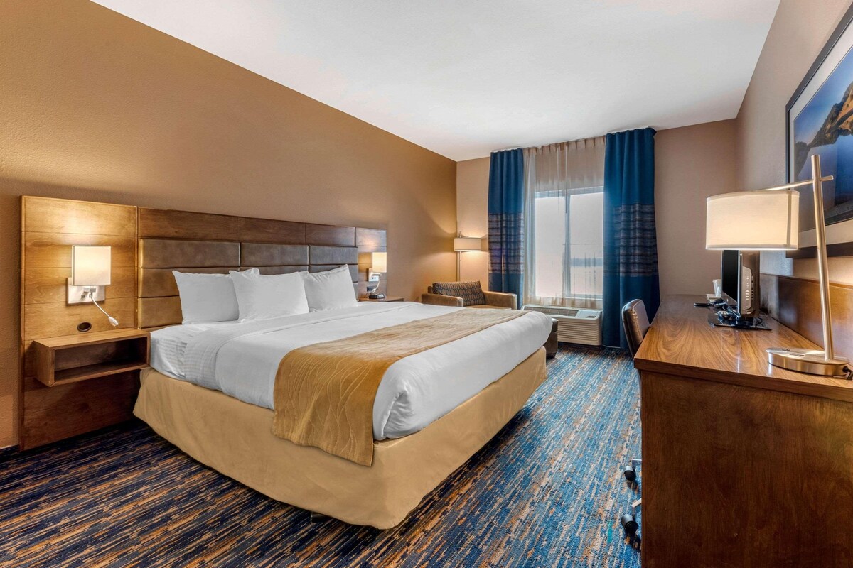 A hotel room with a large bed, bedside tables, a desk, a chair, and a window with curtains.