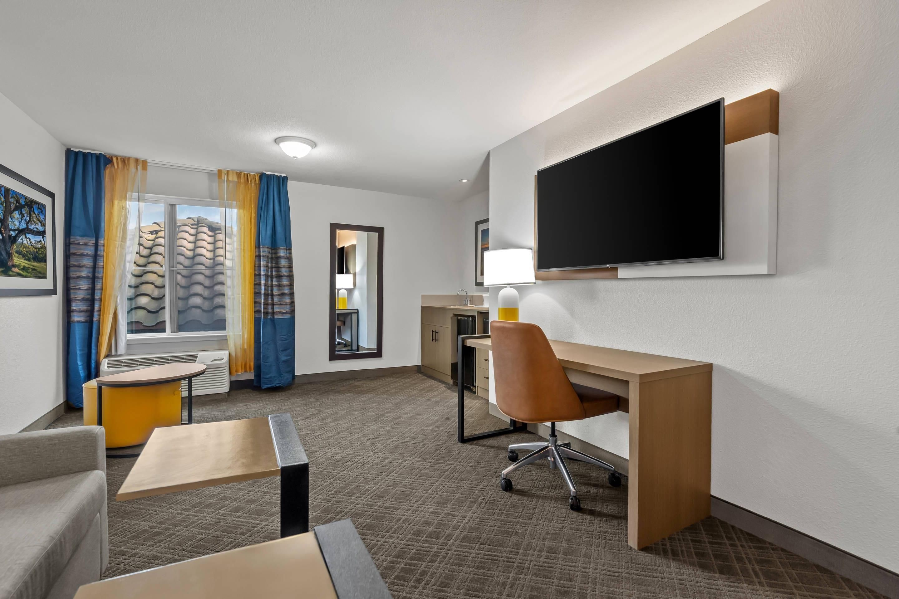 A hotel room with a desk, chair, TV, and a view of the outdoors.