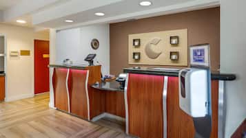 A reception area with a wooden reception desk, a clock, a hand sanitizer dispenser, and a sign instructing to sanitize hands.