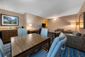 Et hotelværelse med spisebord, stole, sofa, fjernsyn og et maleri på væggen.