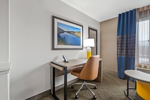 A hotel room with a desk, chair, lamp, and a view of a lake through the window.