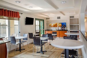 A modern dining area with tables and chairs, a kitchen area with a counter and appliances, and a television mounted on the wall.
