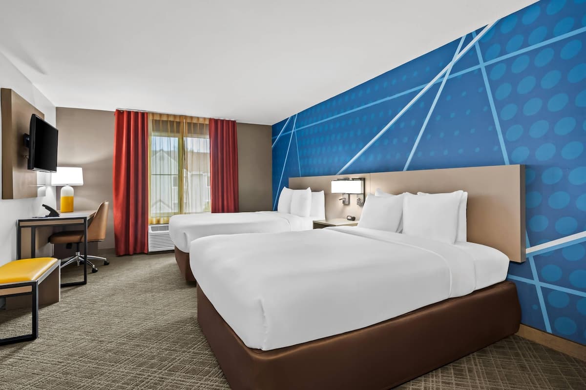Habitación de hotel con una cama grande, dos mesitas de noche, un escritorio con una silla, un televisor y una ventana con cortinas.