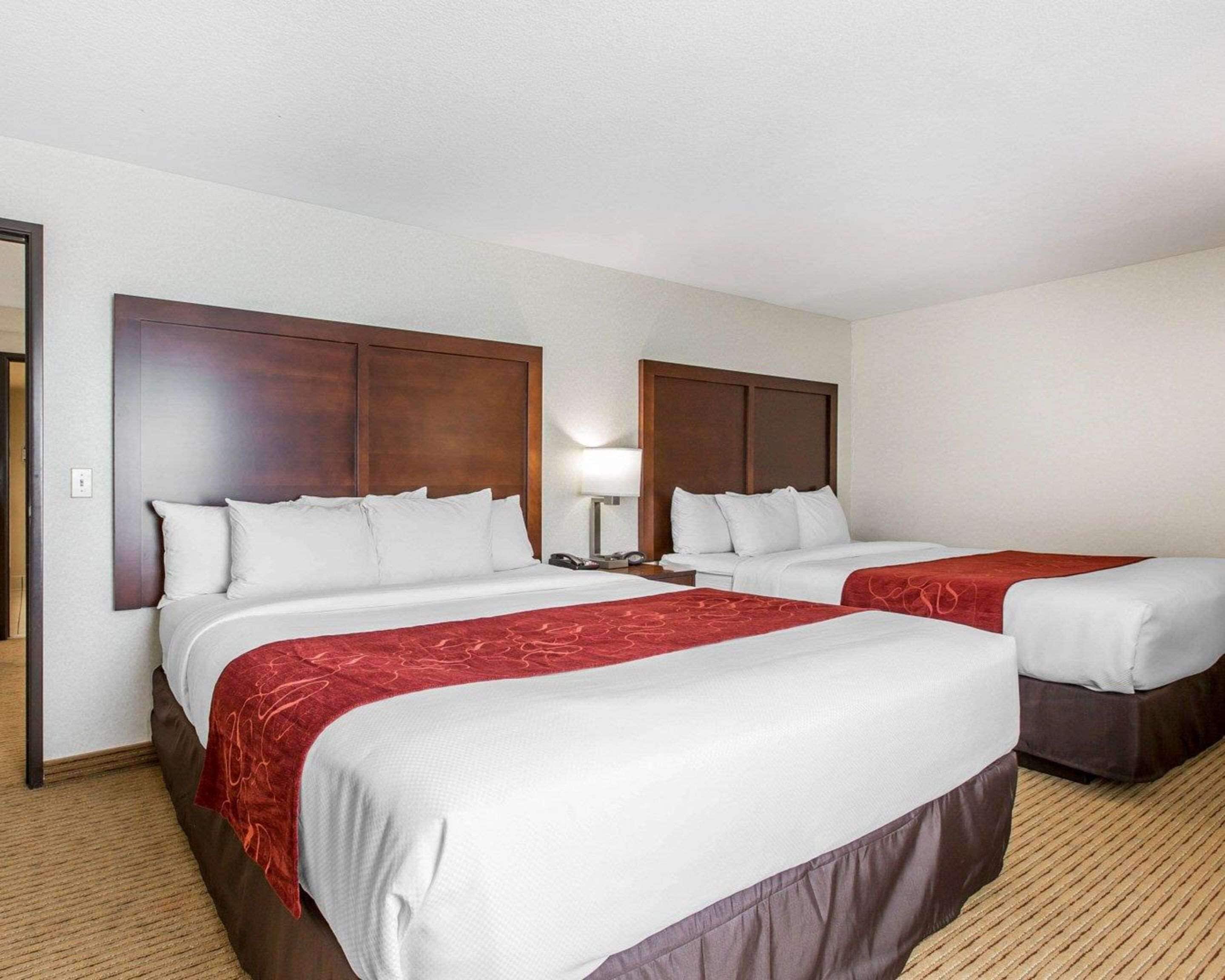 A hotel room with two beds, each with a wooden headboard, white bedding, and a red accent.