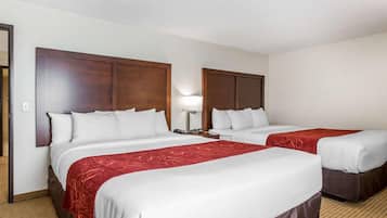 A hotel room with two beds, each with a wooden headboard, white bedding, and a red accent.