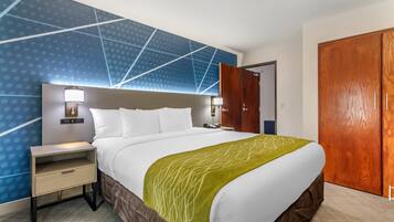 A hotel room with a large bed, a nightstand with a lamp, a wooden wardrobe, and a blue patterned wall.