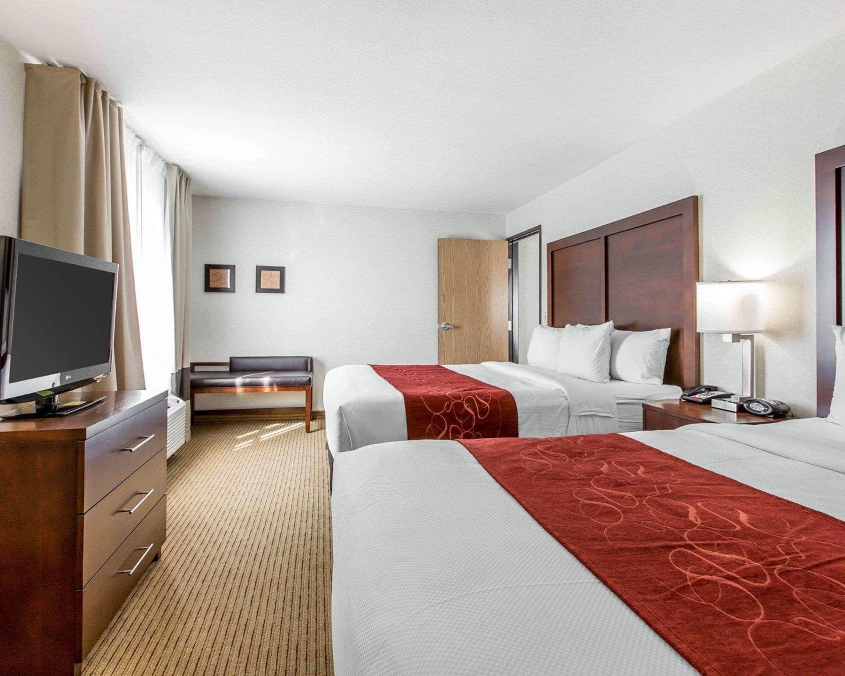 A hotel room with two beds, a TV, a desk, a chair, a wardrobe, and a bedside table with a lamp.