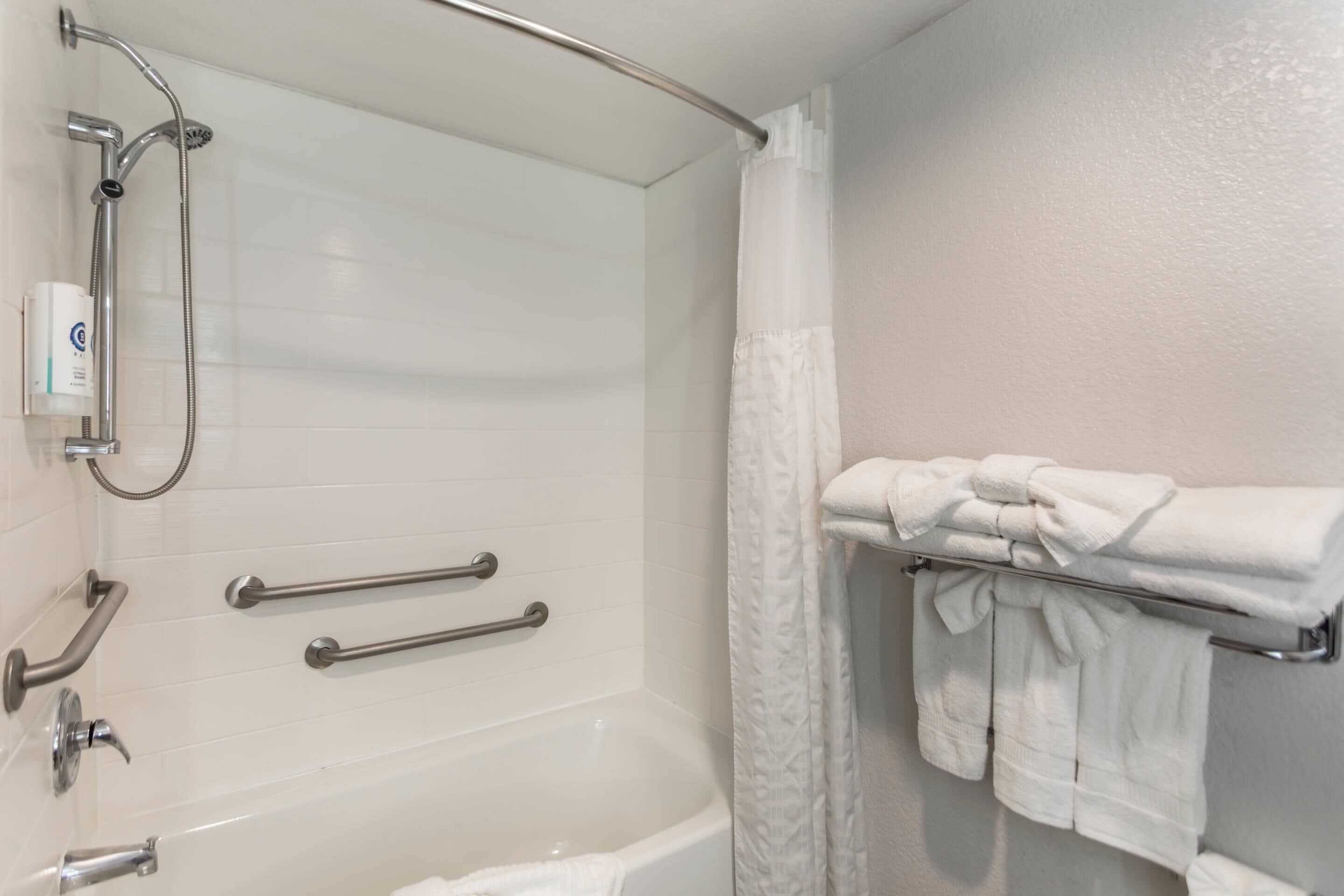 A bathroom with a white bathtub, grab bars, a showerhead, and a towel rack with folded towels.