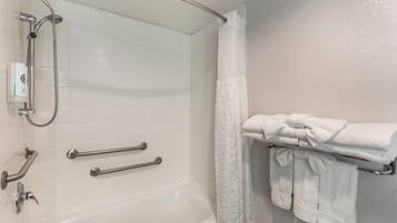 A bathroom with a white bathtub, grab bars, a showerhead, and a towel rack with folded towels.