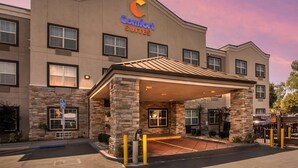 A Comfort Suites hotel with a stone facade, a covered entrance, and a parking area. - Comfort Suites Downtown Sacramento (Sacramento)
