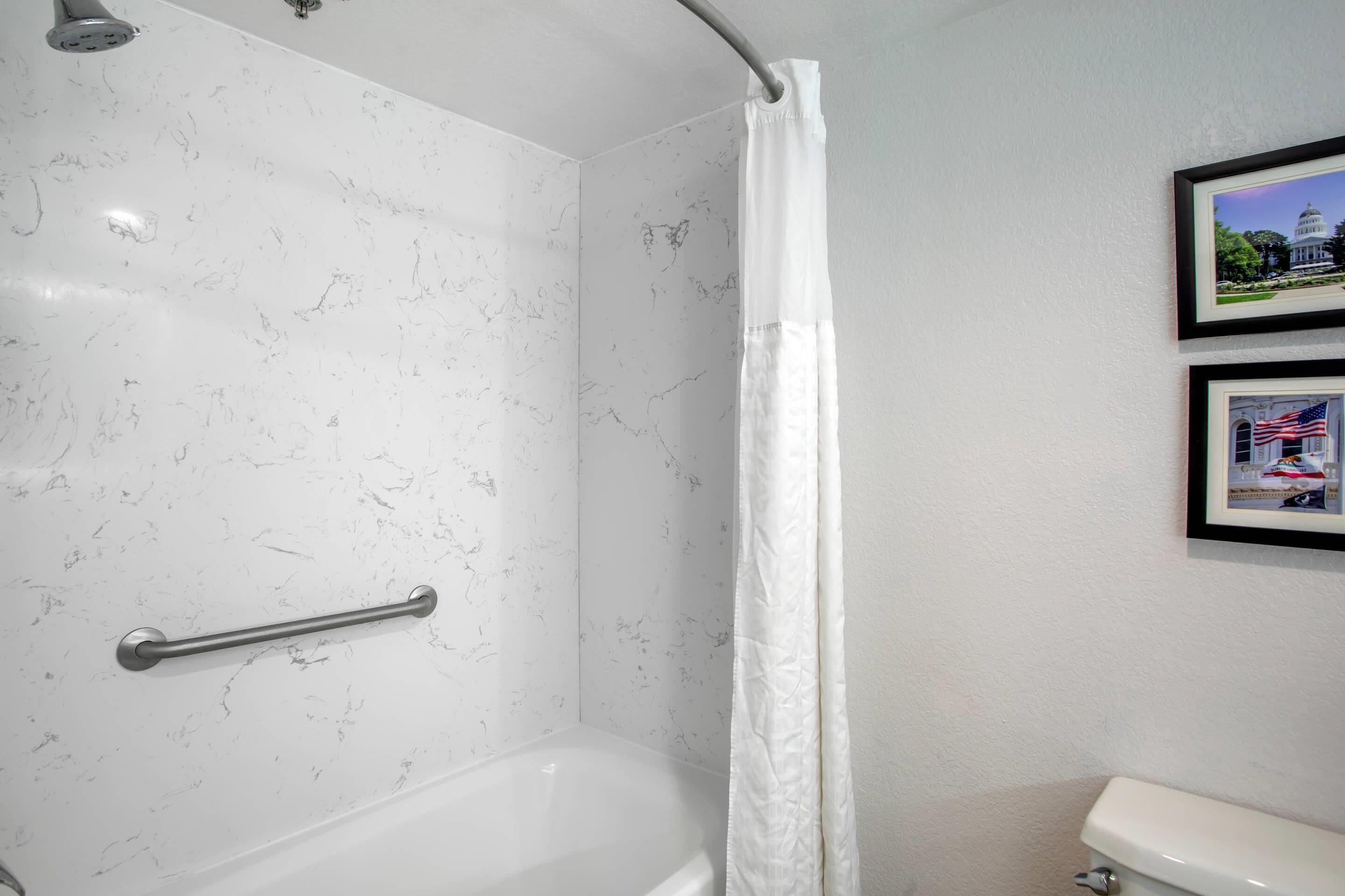 Un baño con pared de mármol blanco, una bañera, un inodoro y una cortina de ducha.